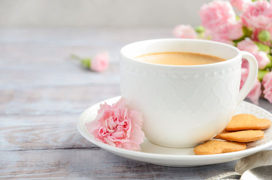 Cup of fresh morning coffee with pink carnation flowers on a wooden background. Valentine's day concept.