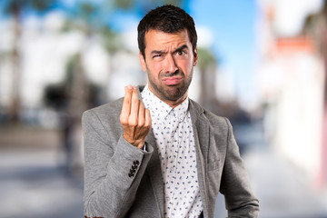 Handsome man making money gesture on unfocused background