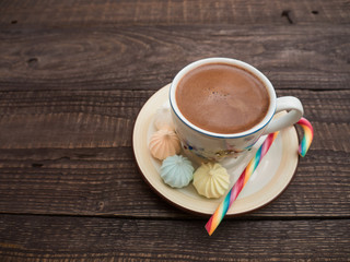 Cocoa with foam, sweet candy and colored bisse on a wooden table