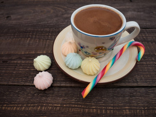 Cocoa with foam, sweet candy and colored bisse on a wooden table