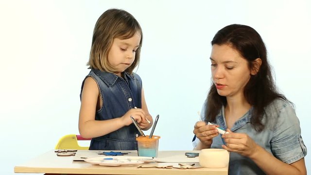 Shooting in the studio on a white background. A child, a funny girl, learns to draw. Mom shows you how to colorize. They are wearing a blue denim dress.