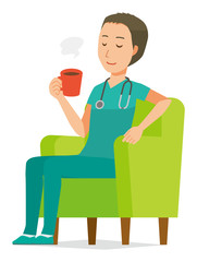 A male doctor wearing a green scrub sits on the sofa and is drinking coffee