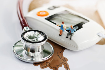 Miniature people sitting on  glucose meter of diabetes and stethoscope  on world map. Healthcare,...
