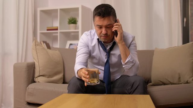 man drinking whiskey and calling on smartphone