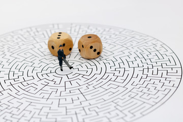 Miniature people: Businessman standing on center of maze with dice. Concepts of finding a solution, problem solving and challenge.
