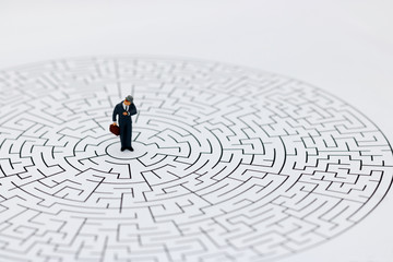 Miniature people: Businessman standing on center of maze with look at watch.. Concepts of finding a...