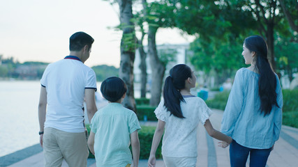 Obraz premium Rear view of Asian family smiling & walking on waterfront promenade at dusk