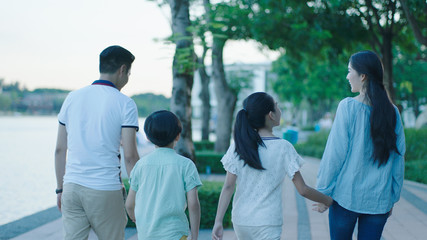 Rear view of Asian family smiling & walking on waterfront promenade at dusk