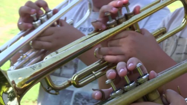 closeups footage as three boys trumpets. We can see their fingers as they trumpeting. The clip was made with handheld camera  