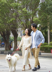 Asian couple laughing while walking dog outdoor in garden