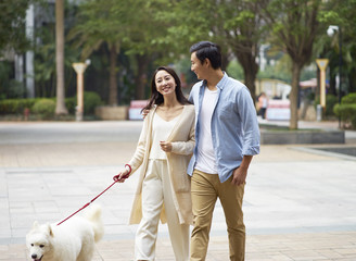 Asian couple laughing while walking dog outdoor in garden