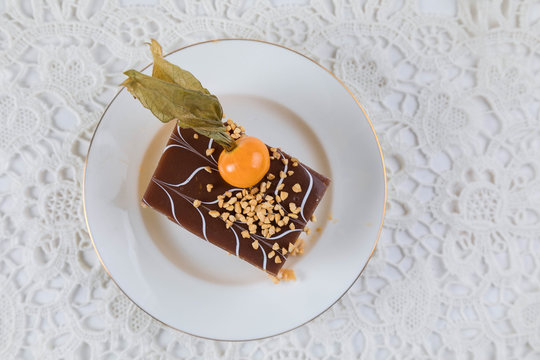 A piece of brown pie decorated with berry physialis on a white plate. The table is decorated with white affective tablecloth