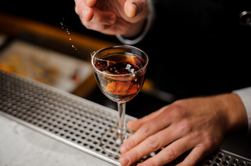 Mans hand holding a glass with splashing alcoholic drink with a slice of orange