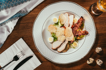 view of ham slices with fried meat and some boiled eggs on plate over table with fork and knife on napkin