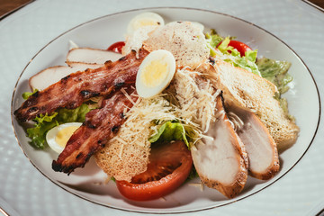 Close-up view of delicious salad with chicken meat, bacon, eggs and cheese dressing served on white plate