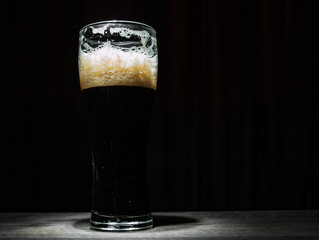Tall glass of dark beer over a dark background