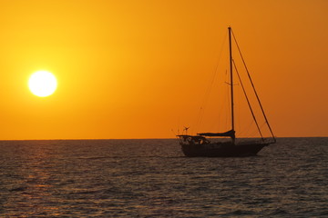 Naklejka premium sail boat sunset on ocean red orange sinking sun in sea