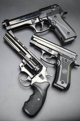 three shiny black pistols on a black background.