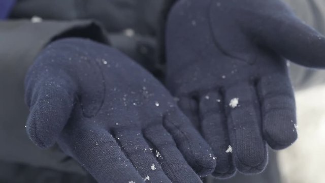 Woman enjoys snowfall and looks at small snowflakes on her blue gloves.
