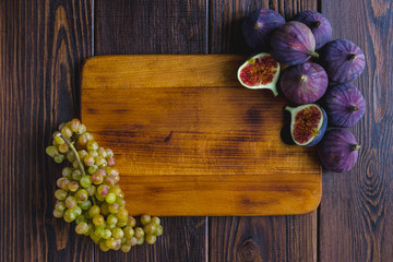 Wooden kitchen board with fig fruits and grapes on it.
