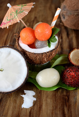 Tropical fruits: longan, rambutan and papaya ball-shaped pieces are lying in coconut. Cocktail ingredients