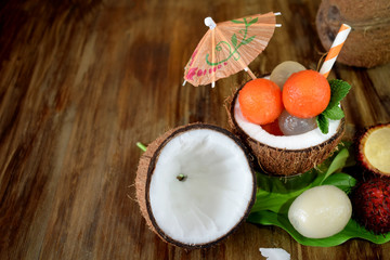 Tropical fruits: longan, rambutan and papaya ball-shaped pieces are lying in coconut. Cocktail ingredients