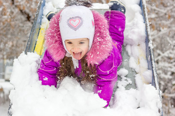 Kid girl on children slide at snowy winter day.