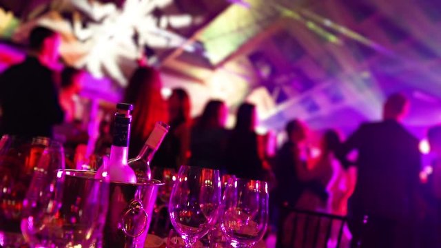 A youth party in a restaurant or a nightclub, banquet tables with alcohol and food against the background of silhouettes of dancing people, stage light and purple fill