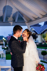 Fototapeta premium The bride smiles and holds a wedding bouquet in her hands and her husband touches her face gently