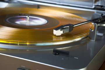 Modern, inexpensive turntable playing a gold colored vinyl record.