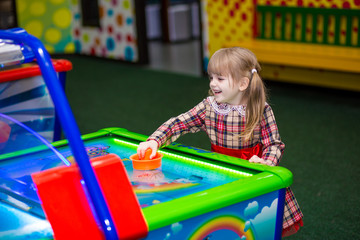 Fototapeta na wymiar Happy smiling little girl play air hockey. Funny child having fun in play room