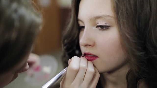 makeup artist paints lips to the teenager girl in the beauty salon