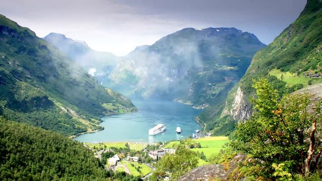 Beautiful time lapse video of mountains in a fjord with a ferry, boat, shadows, clouds moving in Geiranger, Norway