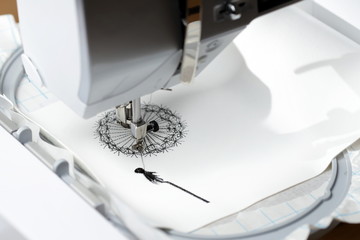 embroidery with embroidery machine - dandilon on white leatherette - view on embroidery process, machine head and hoop from left