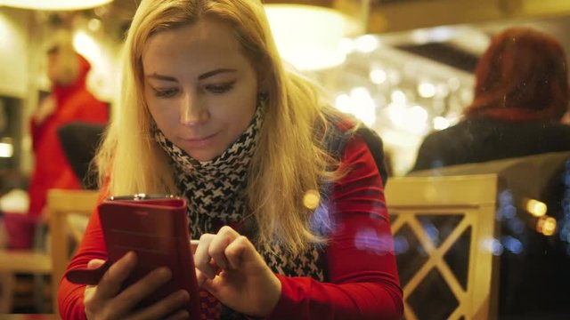 Young direct girl looks photos by mobile phone at cafe house during cold winter holidays  
