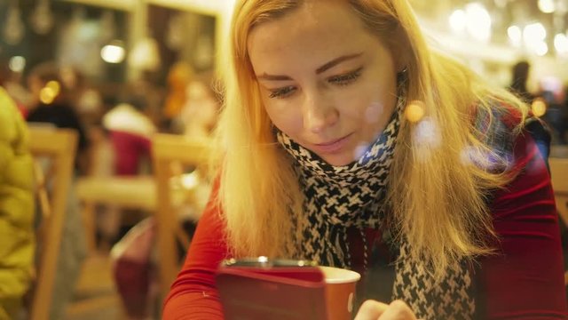  Direct young smiling girl looks photos by mobile in cafe house close-up during cold winter holidays  
