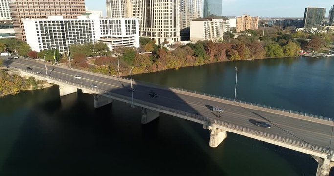 A slow reverse aerial view of traffic flowing over the S Congress Avenue Bridge over the Colorado River in downtown Austin, Texas on an early autumn evening.  	