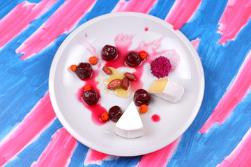 Cheese, camembert on a white plate, pop art, fruit and cheese on a blue rose background, peanuts, honey, canned cherries, sauce sauce on a plate