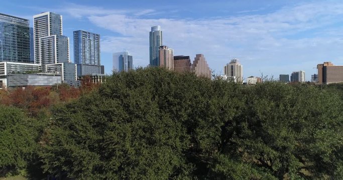 A dramatic rising aerial view revealing the Austin city skyline as seen from Vic Mathias Shores Park on a late Autumn sunny day as a jogger runs on the trails.  	
