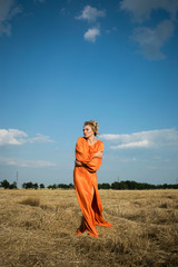 Beautiful and passion woman with sexy legs in a long orange dress in the field.  Sexy blond girl with amazing legs on tha background of the field