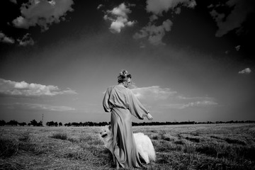 Portrait of beautiful woman and dog in the field. Samoyed and lady in long dress are walking in the field