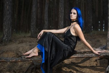 Beautiful woman with dark blue hair dressed in black dress in the magic forest