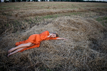Beautiful blond in a long dress with beautiful legs lies in a field on a hay