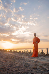 Passion woman with beautiful long legs in a long orange dress at sunset