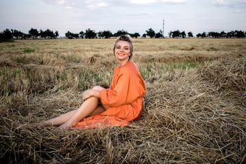Pretty woman with charming smile with beautiful legs in the field on a hay