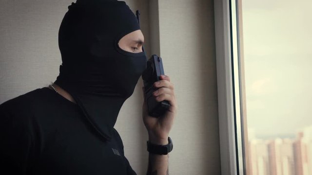 Armed male terrorist with a walkie-talkie tracks down the victim out the window