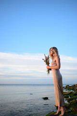 fashion woman  in long dress with dry flowers in hands on a beach