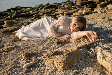 a young woman with a languid look in a white dress lies on the rocks on the seashore. Angry bride