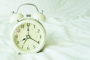 Closeup alarm clock on white bed in bedroom for wake up time concept