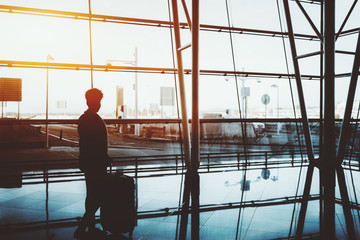 Silhouette of curly black female standing indoors with a huge rolling bag in front of panoramic...